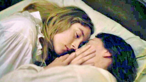 Blonde and brunette lesbians cuddling tenderly face-to-face in bed wearing sheer nightgowns