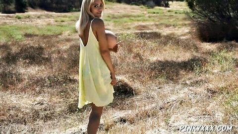 Blonde woman in yellow dress holding massive fake tits outdoors, big tits fetish