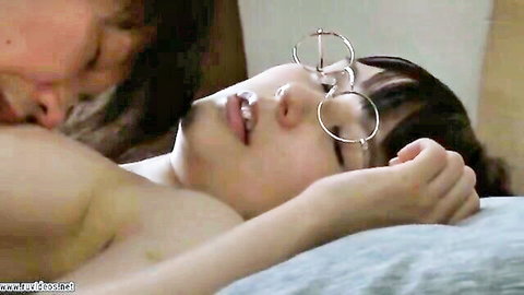 Muscular man kisses topless Japanese girl with glasses and hoop earrings lying on bed
