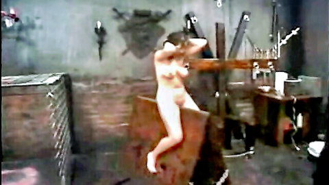 Curly blonde nude woman tortured in BDSM dungeon, tits and pussy exposed