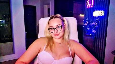 Blonde camgirl Janemiss in pink bra, smiling seductively with glasses