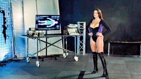 Sexy superhero babe in tight purple bodysuit and thigh-high boots poses confidently in sci-fi lab with body scan monitor