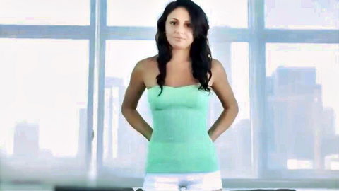 Sexy brunette in green tube top and white shorts posing confidently by city window