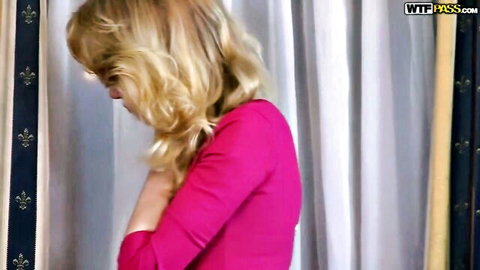 Blonde babe in tight pink dress teasing with hand on chest in luxury bedroom