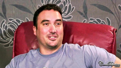 Bearded man smirking while lounging in red leather chair on adult site