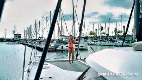 Blonde skinny babe in red bikini poses teasingly on yacht deck in marina