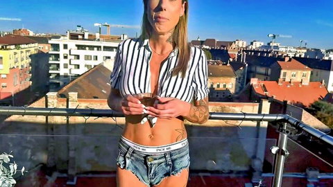 Blonde tattooed babe in unbuttoned striped shirt flashing abs and tiny pink denim shorts on balcony