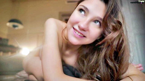 Smiling topless girl with perky tits and wavy hair teases seductively on webcam