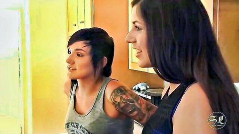 Tattooed pixie-cut babe in tank top smiles at long-haired beauty in locker room tease