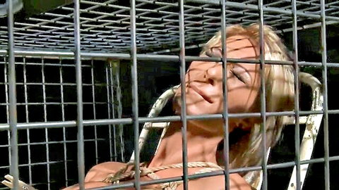 Blonde BDSM slave bound topless in cage for sub training