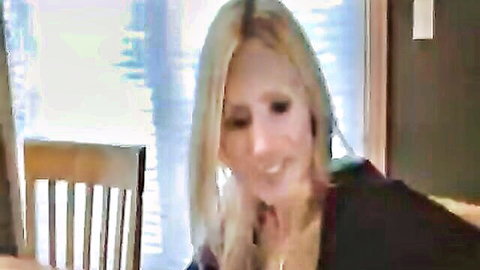 Naughty blonde MILF with long hair smiling teasingly in bedroom