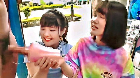 Two smiling Asian girls use pink fleshlight on thick erect cock in public outdoor setting