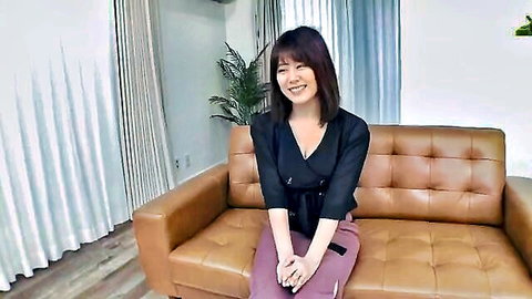 Smiling Asian woman in black wrap top showing cleavage, sitting casually
