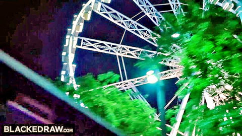 Illuminated Ferris wheel spinning at night with bright lights and green foliage glow
