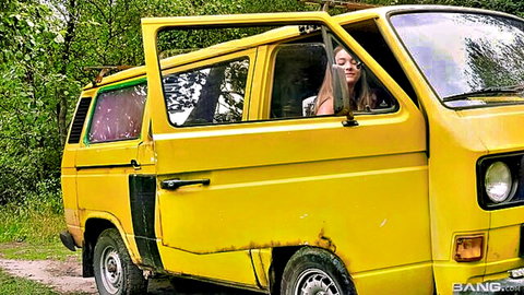 Young skinny brunette teen smiling from open door of yellow VW van outdoors