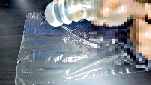 Hand squeezing clear plastic bag filled with thick white cum on black surface