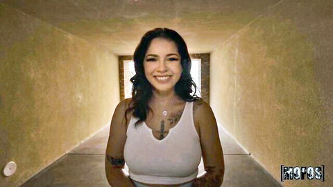 Tanned brunette with tattoos smiling in tight white tank top showing deep cleavage