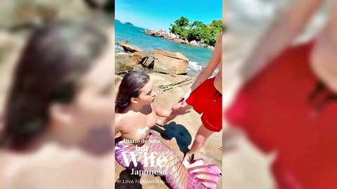 Topless Asian mermaid in purple tail holds hands with man on sunny beach