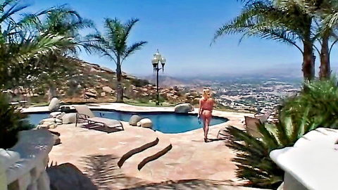Blonde beauty in orange bikini strolling by luxury poolside