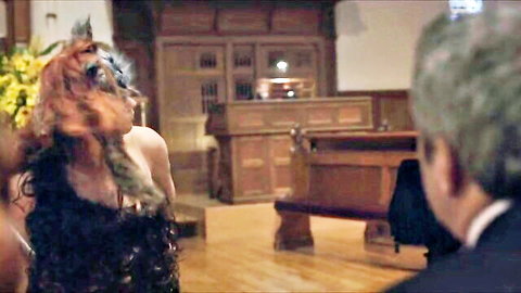 Redhead in black dress and feathered mask, seductive pose with older man