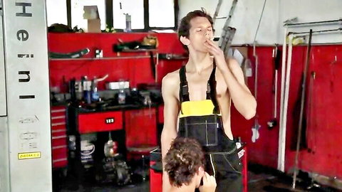 Shirtless mechanic in overalls gets blowjob from kneeling brunette in garage while smoking