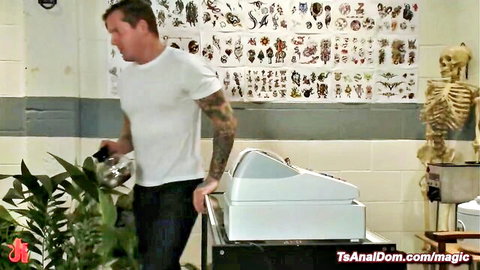 Tattooed muscular man in white tee watering plants by washing machine in laundromat tattoo parlor