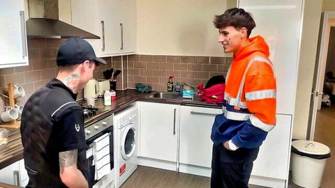 Tattooed repairman chats with curly-haired roadman in workwear near washing machine
