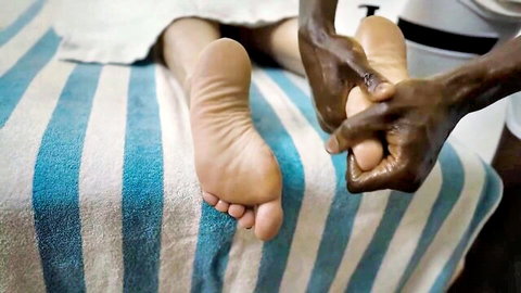 Black man massages and oils bare soles of sexy white woman's feet on massage table