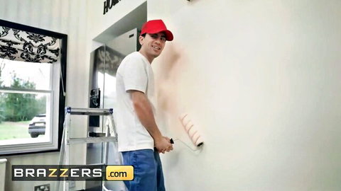 Handsome painter in red cap and white tee rolling paint on wall on ladder in Brazzers scene