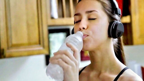 Brunette in headphones sips water teasingly in black top, wet lesbian passion vibe