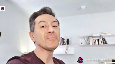 Handsome gray-haired man in maroon shirt smirking in modern bookshelf room