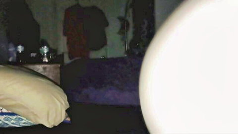 Blurry dimly lit bedroom with purple bed yellow pillow nightstand bottles and clothes rack