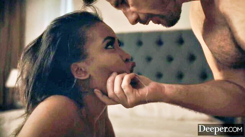 Bearded white man grips ebony woman's face intensely on bed in steamy interracial encounter