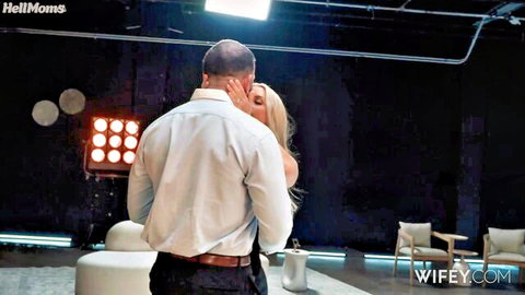 Hot blonde MILF wife passionately embraced and kissed from behind by suited man in studio