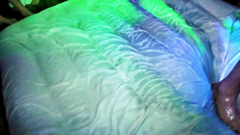Neon green lit white sheets with bare foot and toes on bed in dimly lit room