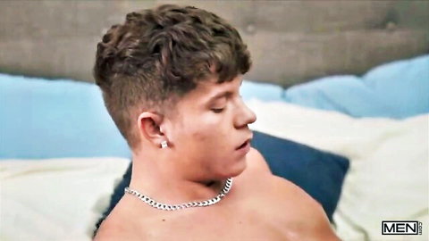 Handsome young twink with curly hair lying shirtless on bed, seductive side profile