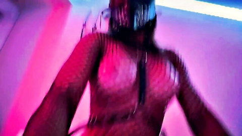 Curvy woman in sheer fishnet bodysuit poses with arms wide flaunting huge tits in neon BDSM glow