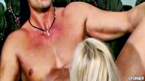 Blonde woman gives deep blowjob to muscular shirtless stud with necklace on couch