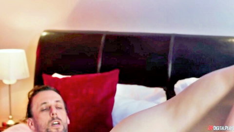 Muscular man lying shirtless in bed with woman's bare thigh beside him in bedroom