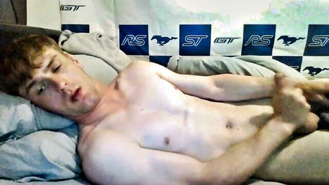 Short-haired ginger twink lying shirtless on bed with hand down pants stroking his cock