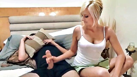 Blonde in white tank top and green skirt gives handjob to man's hard cock on bed