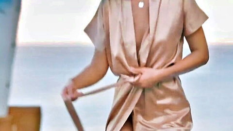 Seductive woman in open silk robe showing cleavage on ocean balcony