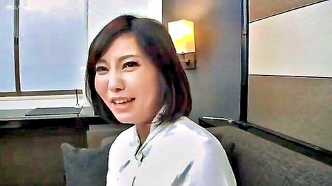 Cute Asian woman with bob haircut smiling seductively in tight white blouse on couch
