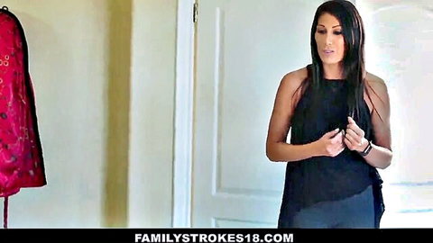 Brunette woman in tight black tank top stands talking in bedroom with red dress hanging