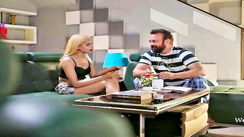 Blonde Indian woman in short skirt chats with older bearded man on sofa