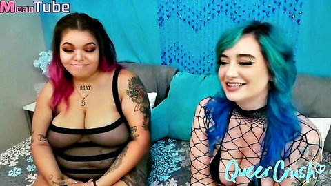 Busty tattooed pink-haired and teal-haired babes exposing tits in sheer fishnet tops smiling on bed