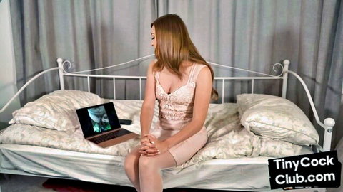 Petite blonde babe in lace dress sits on bed viewing tiny cock on laptop for SPH humiliation