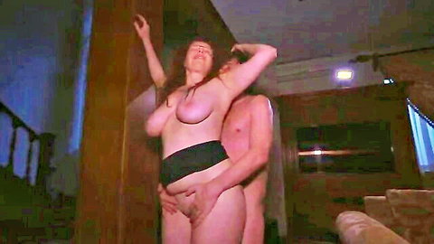 Redhead MILF with huge tits and hairy pussy stands nude against wall as naked man gropes her from behind