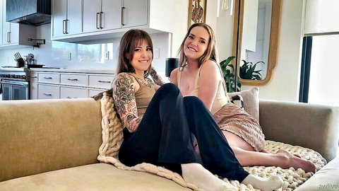Tattooed brunette and busty blonde tease with deep cleavage on cozy couch