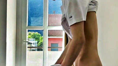 Slim tanned legs teasing with lifted shirt by sunny window view
